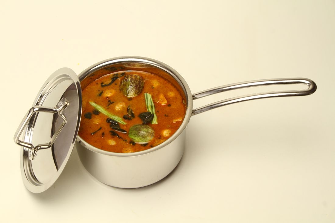 Stainless steel saucepan filled with curry, lid propped against its side