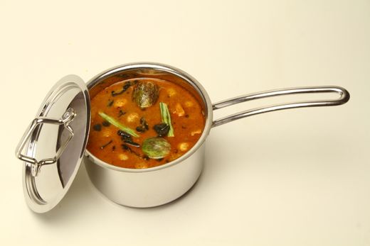 Stainless steel saucepan filled with curry, lid propped against its side