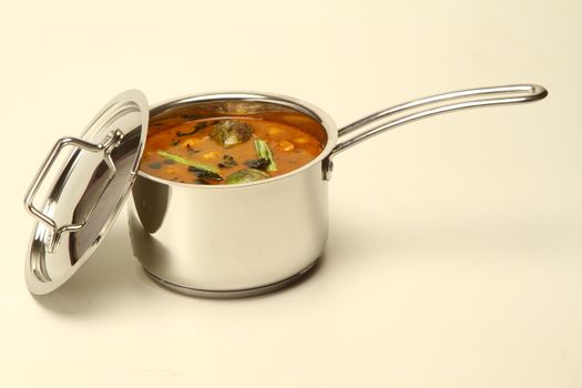 A stainless steel pot filled with traditional South Indian sambar on a neutral background.
