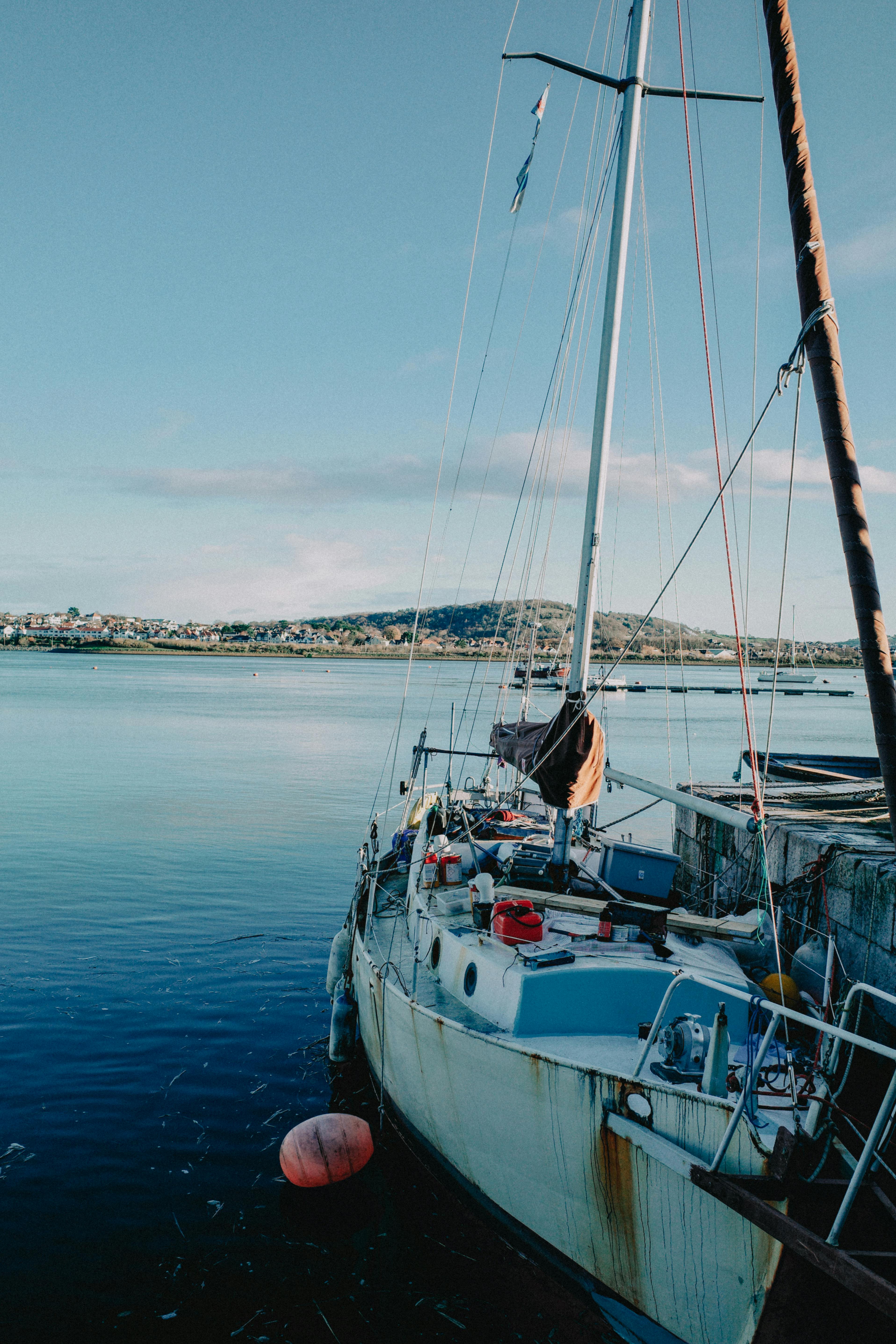 Rustic sailboat moored by a serene shore in Conwy, Wales under a clear blue sky.