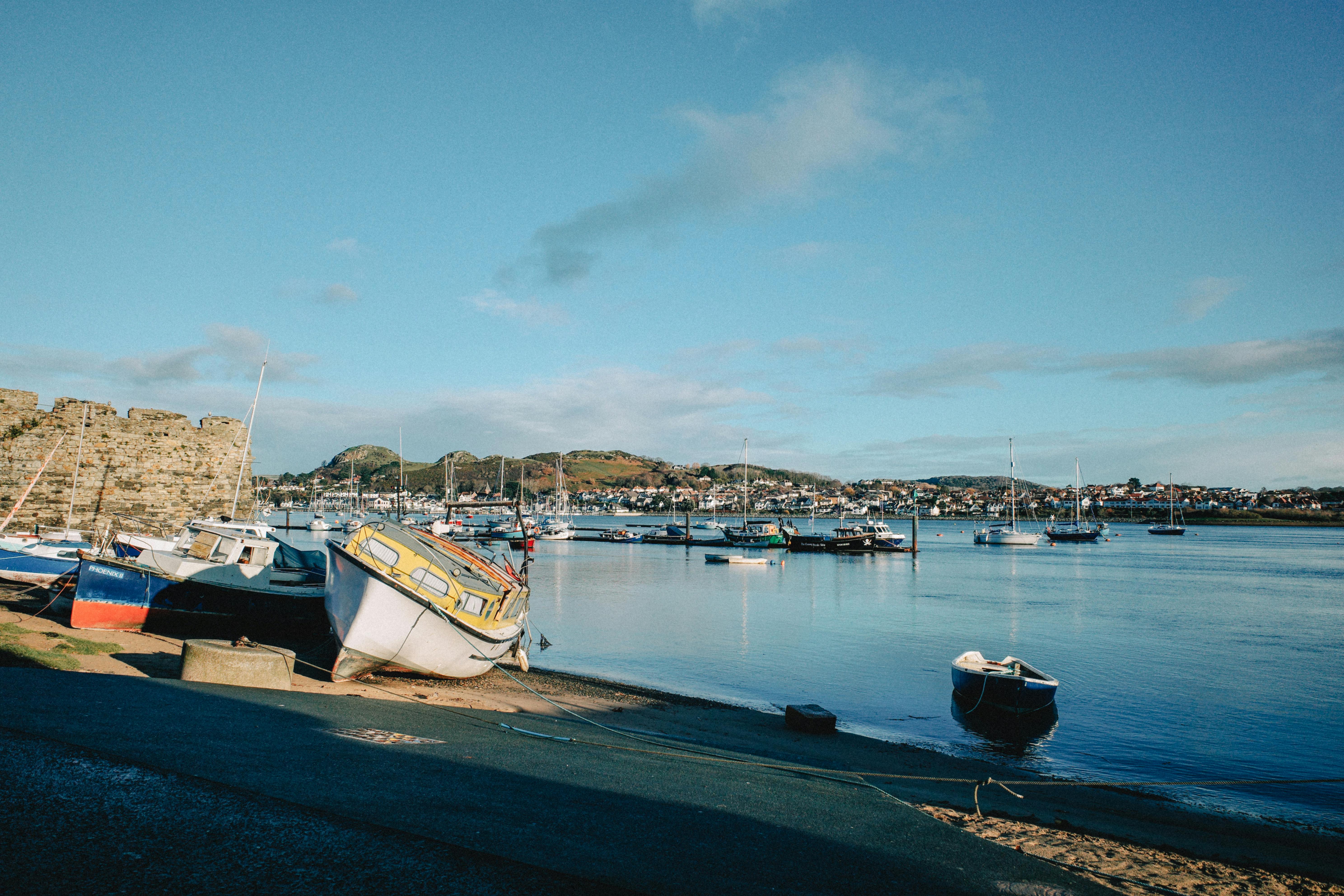 Boats docked at a tranquil harbor in Conwy, Wales during daytime with scenic hills in the background.