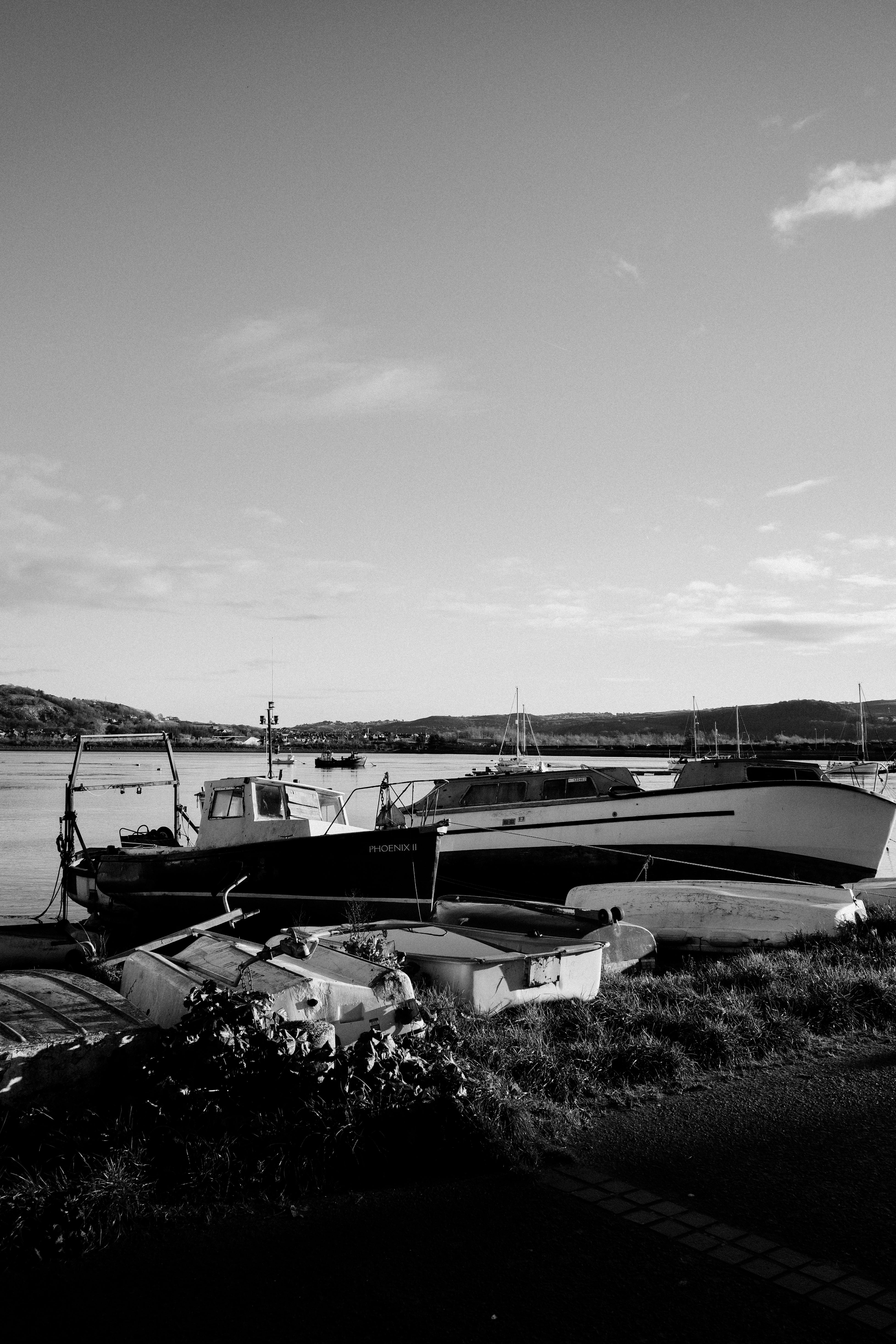Black and white photo of boats docked in Conwy Harbor, Wales, showcasing serene waterfront scenery.