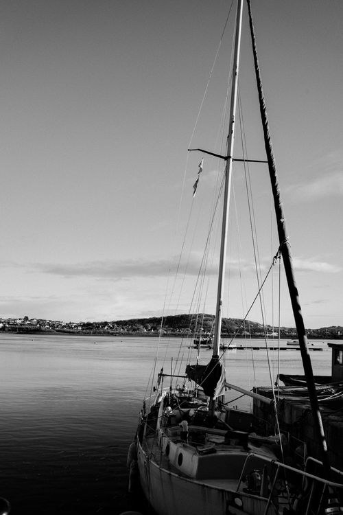 Free Tranquil black and white photo of a yacht docked in Conwy, Wales, with a clear sky and calm waters. Stock Photo