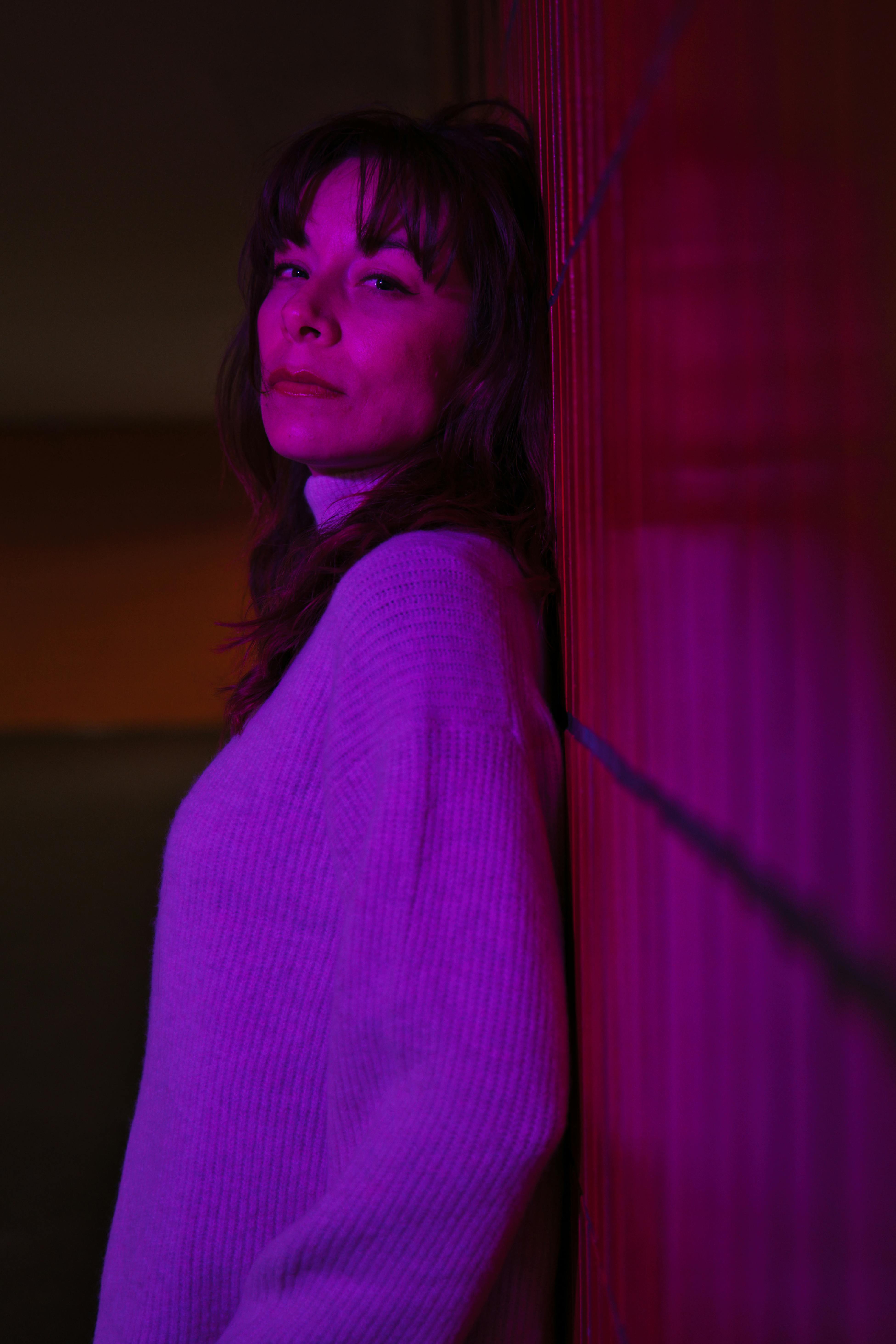 Woman leaning against wall in purple light, creating a moody atmosphere.