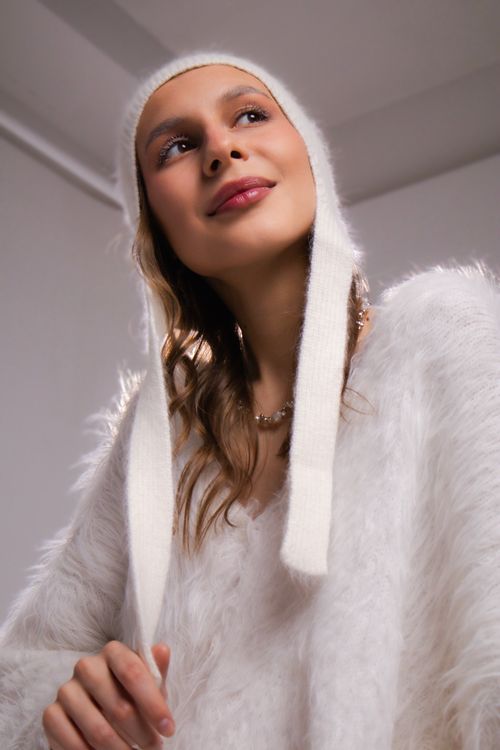 Free Portrait of a stylish woman in a fuzzy white sweater and hat, looking upwards indoors. Stock Photo