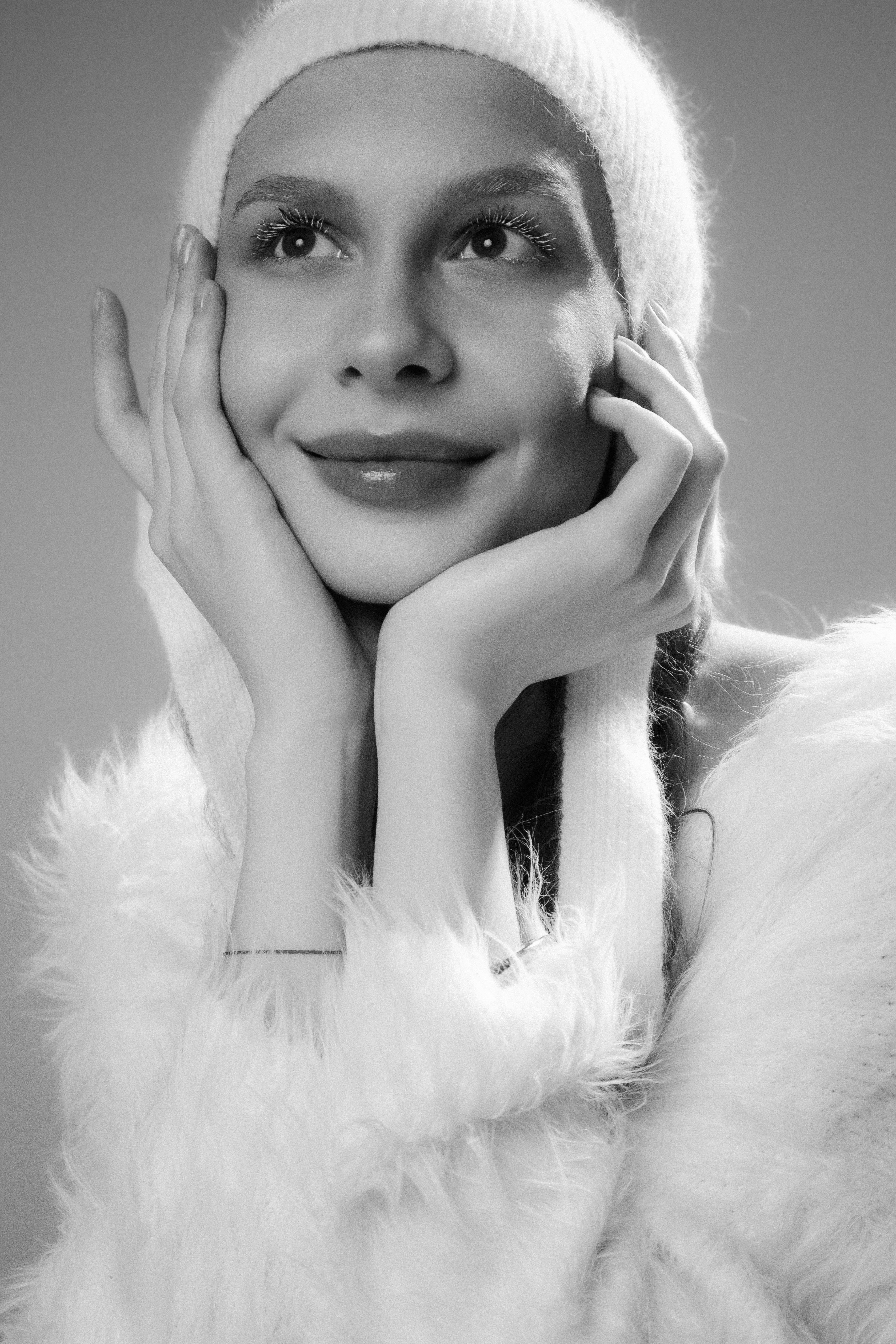 무료 푹신한 코트와 겨울 모자를 쓴 여성이 위를 바라보는 흑백 사진입니다. 스톡 사진