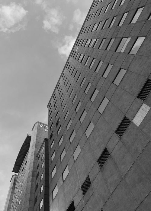 Free A black and white photo of a modern skyscraper with a geometric facade against a cloudy sky. Stock Photo