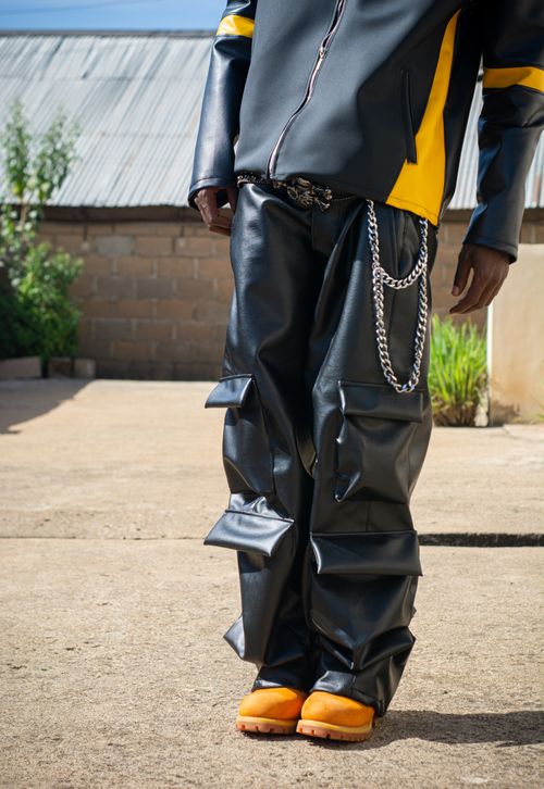 Free Stylish streetwear featuring black baggy leather pants and orange shoes in an outdoor setting. Stock Photo