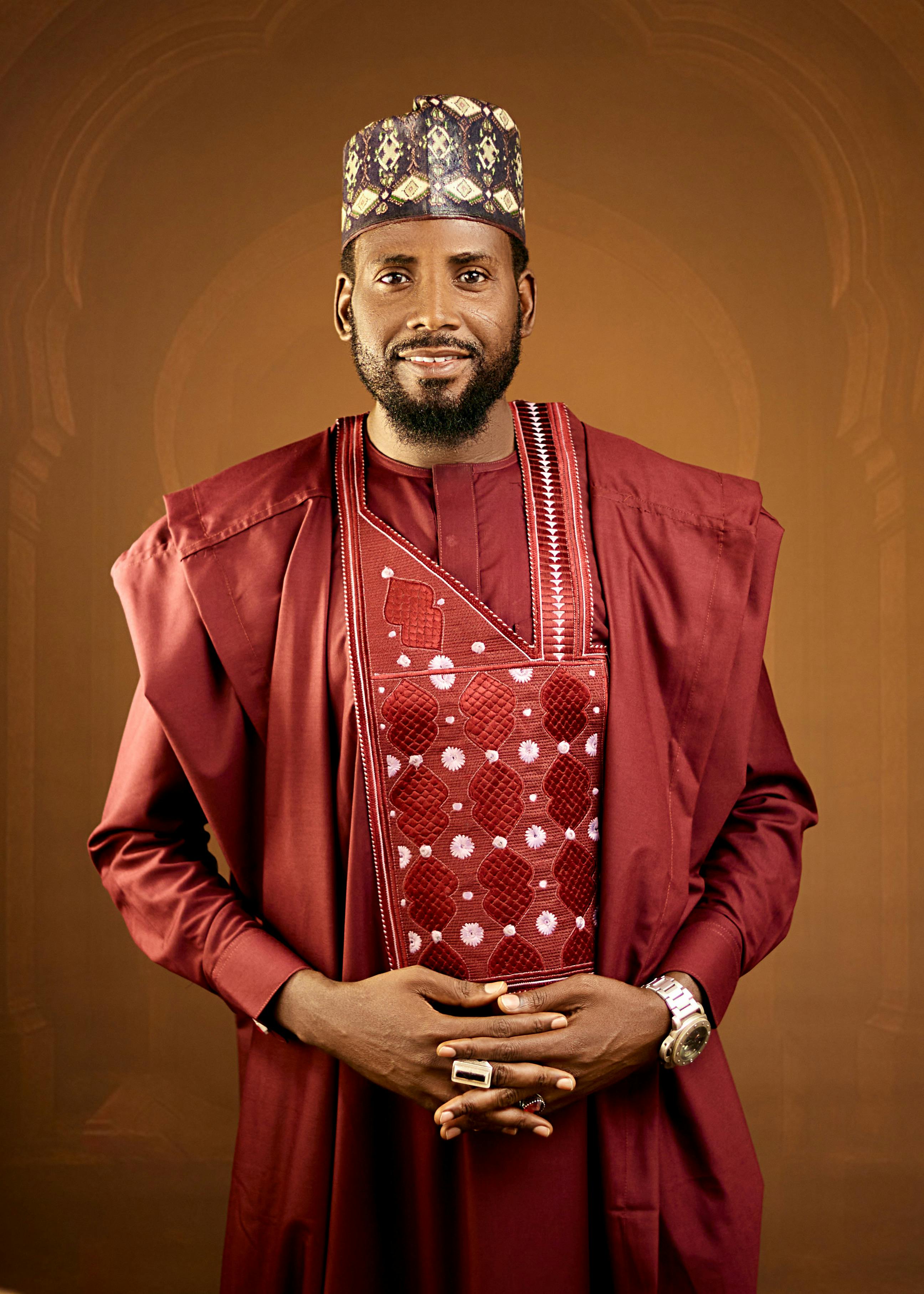 Portrait of a man in traditional African attire against a brown background.