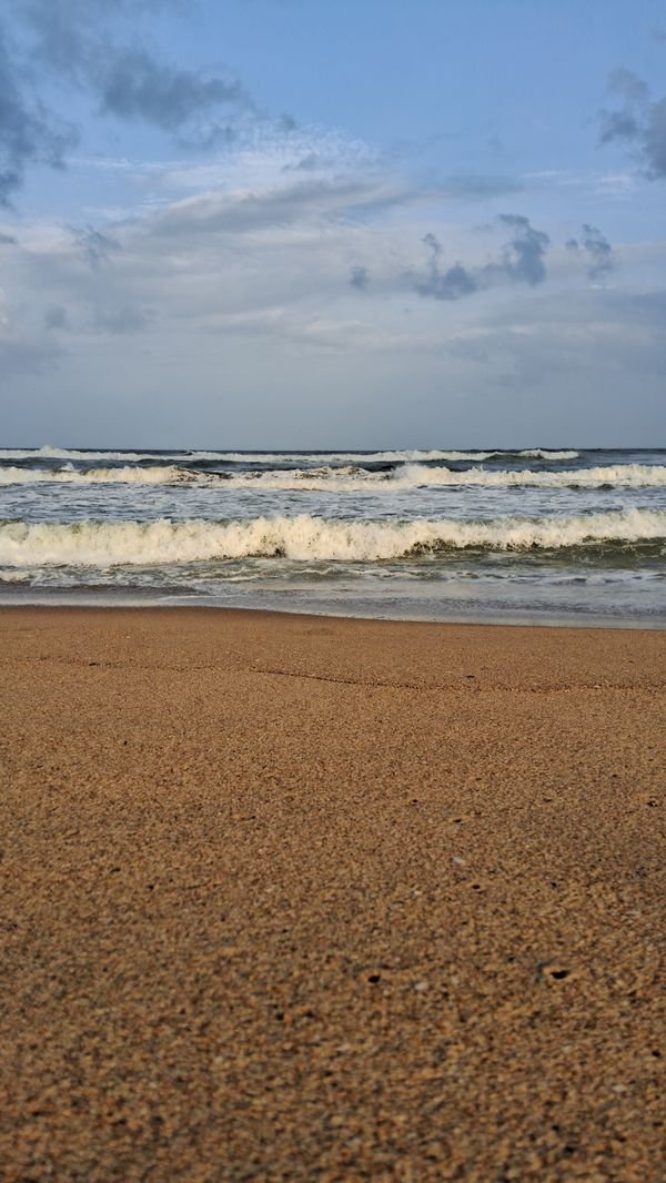 Vista tranquila de ondas suaves do oceano lambendo uma praia de areia sob um céu azul claro.