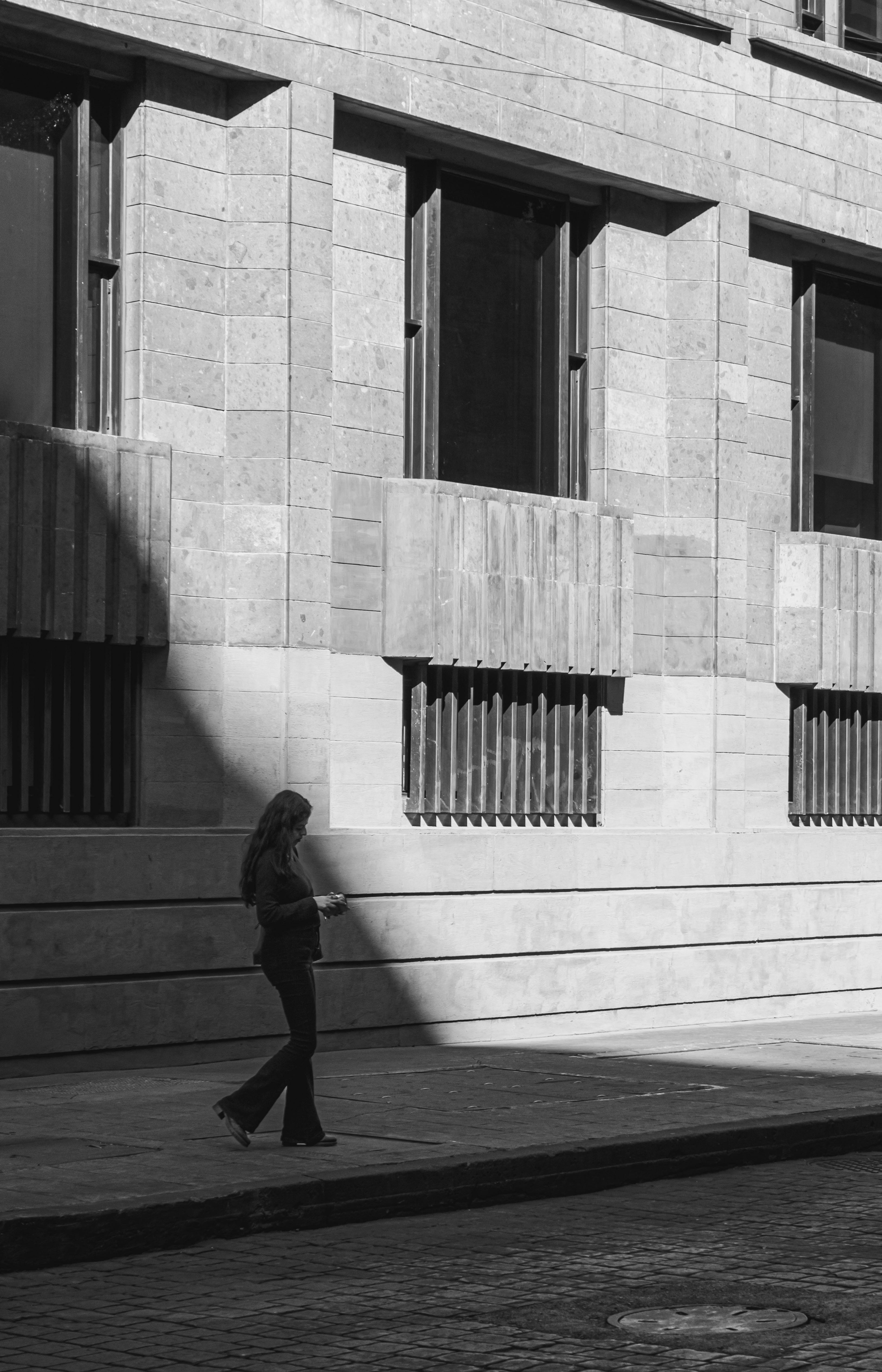 A woman walks by a textured building with dramatic shadows.