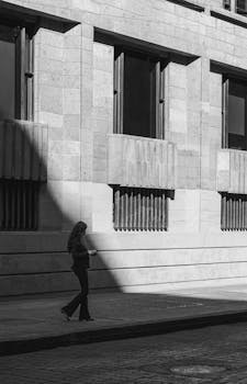 A woman walks by a textured building with dramatic shadows.