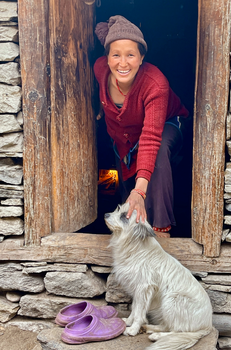 A cheerful Nepali woman pets a dog at a doorway in Karnali Province, Nepal.