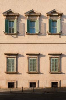 Elegant facade with green shutters in warm sunlight, showcasing classic architecture.