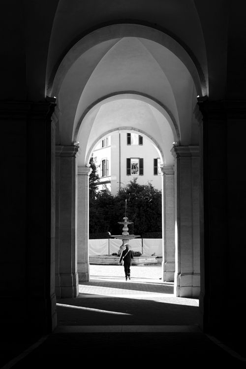 Free Monochrome photo of a person walking through a grand architectural archway. Stock Photo