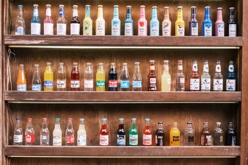 Free A vibrant collection of vintage soda bottles displayed on wooden shelves, showcasing diverse colors and labels. Stock Photo