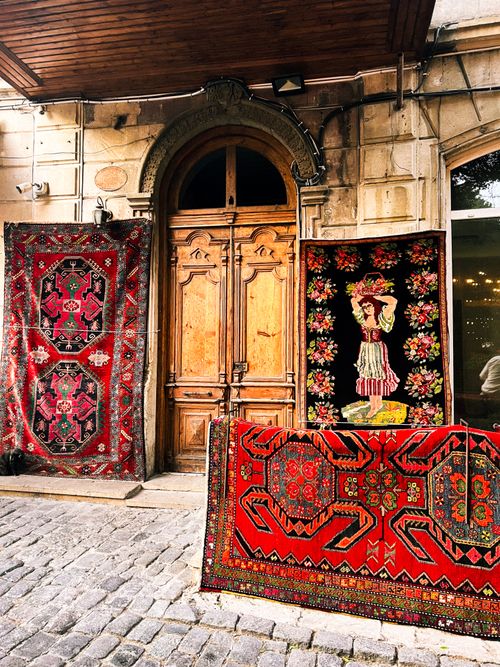 Free Colorful Azerbaijani rugs adorn an old wooden doorway in Baku, showcasing local craftsmanship. Stock Photo