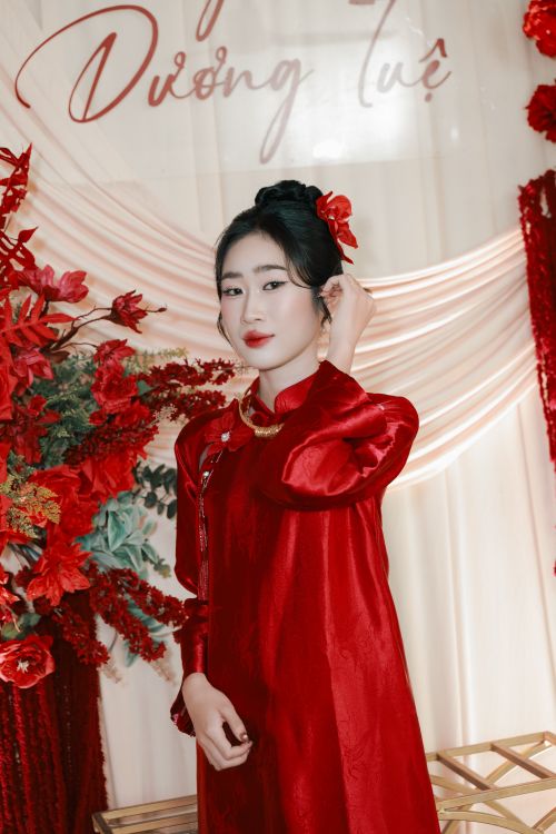 Free Portrait of a woman in a red gown surrounded by vibrant floral decor, exuding elegance and poise. Stock Photo