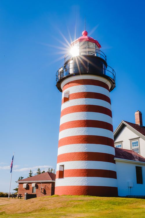 Free Iconic Quoddy Head Lighthouse with sunburst effect in vibrant daylight. Stock Photo