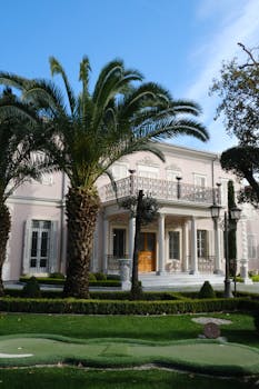 Stunning mansion in İzmir surrounded by lush palm trees under a bright sky.