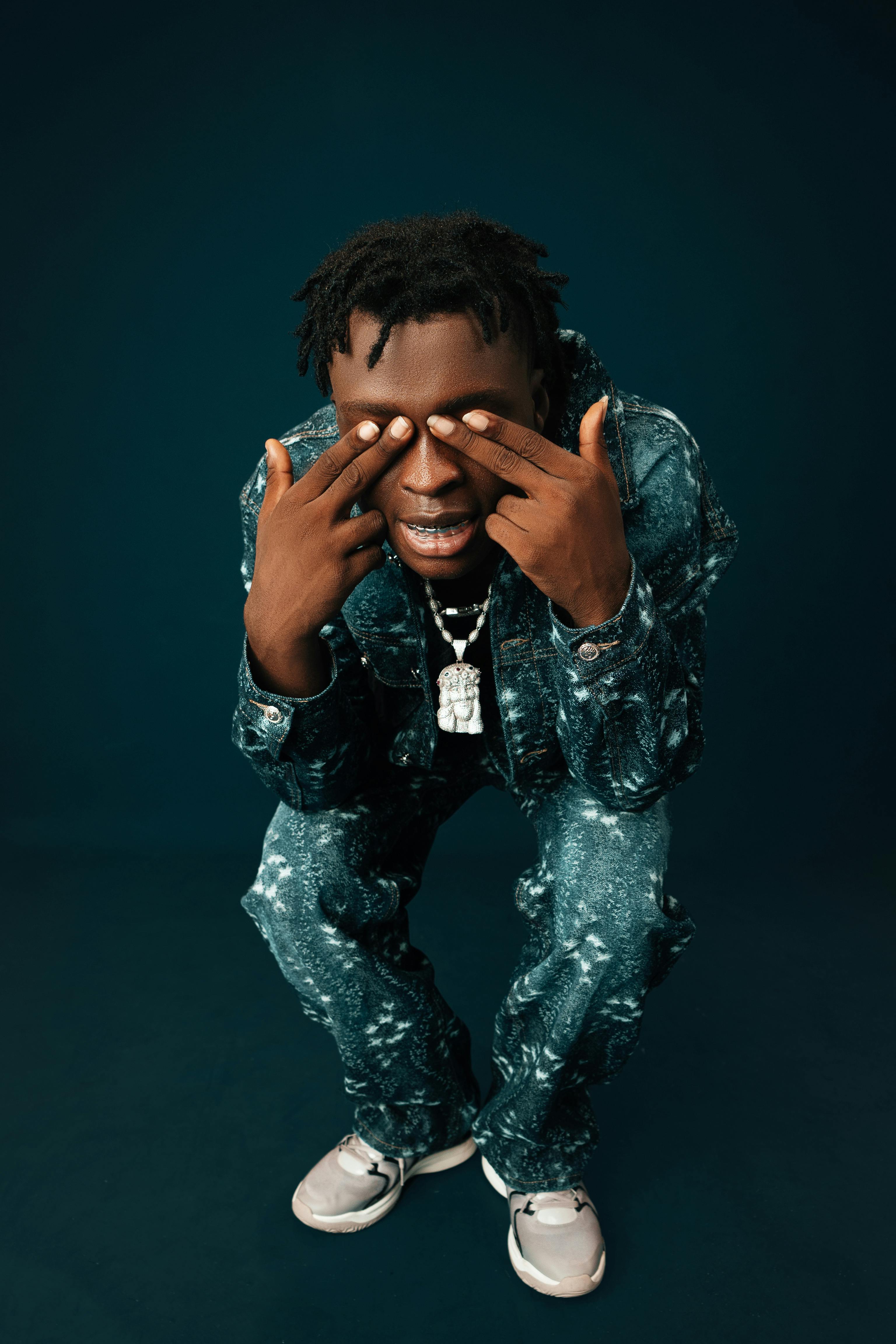 Stylish young black man posing in denim outfit against dark background.