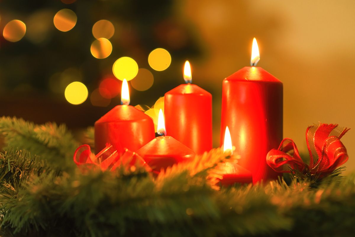 Five lit candles on a mantel beside a small wreath.