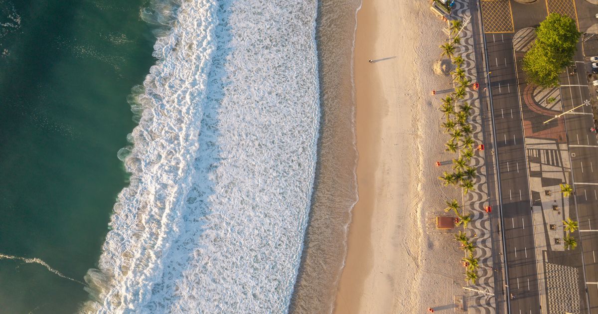Impressionante foto aérea de uma praia do Rio de Janeiro, com a luz dourada do sol realçando as ondas e o litoral.