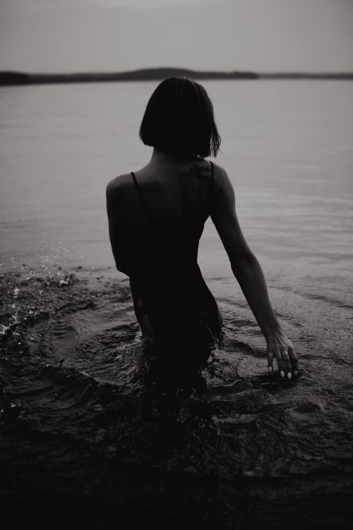 Free A serene black and white image of a woman standing in calm water, creating a reflective and moody atmosphere. Stock Photo