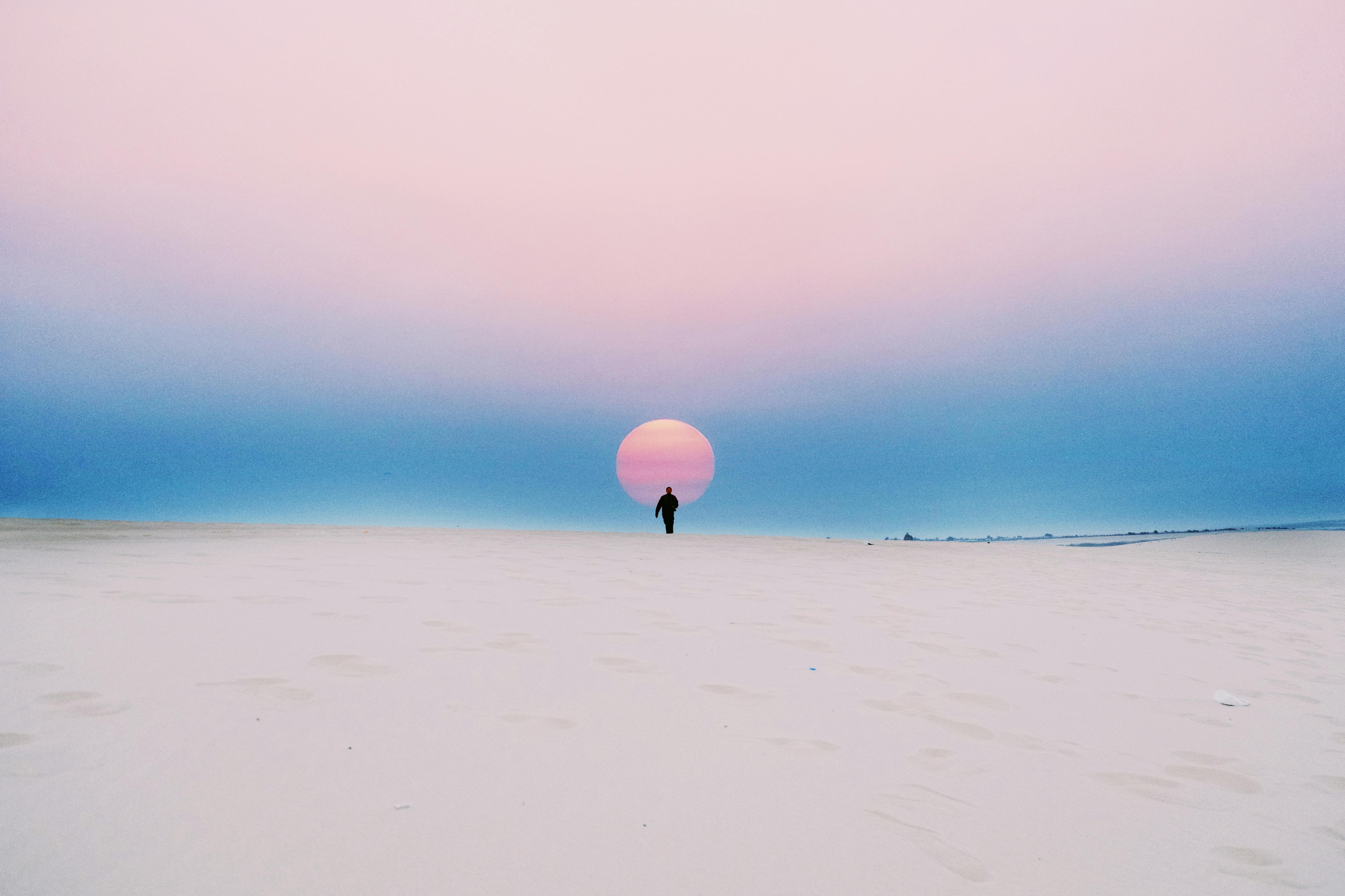 A lone figure walks towards a vibrant sunset on a vast desert landscape, capturing a serene moment of solitude.