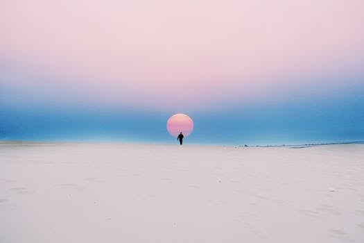 A lone figure walks towards a vibrant sunset on a vast desert landscape, capturing a serene moment of solitude.
