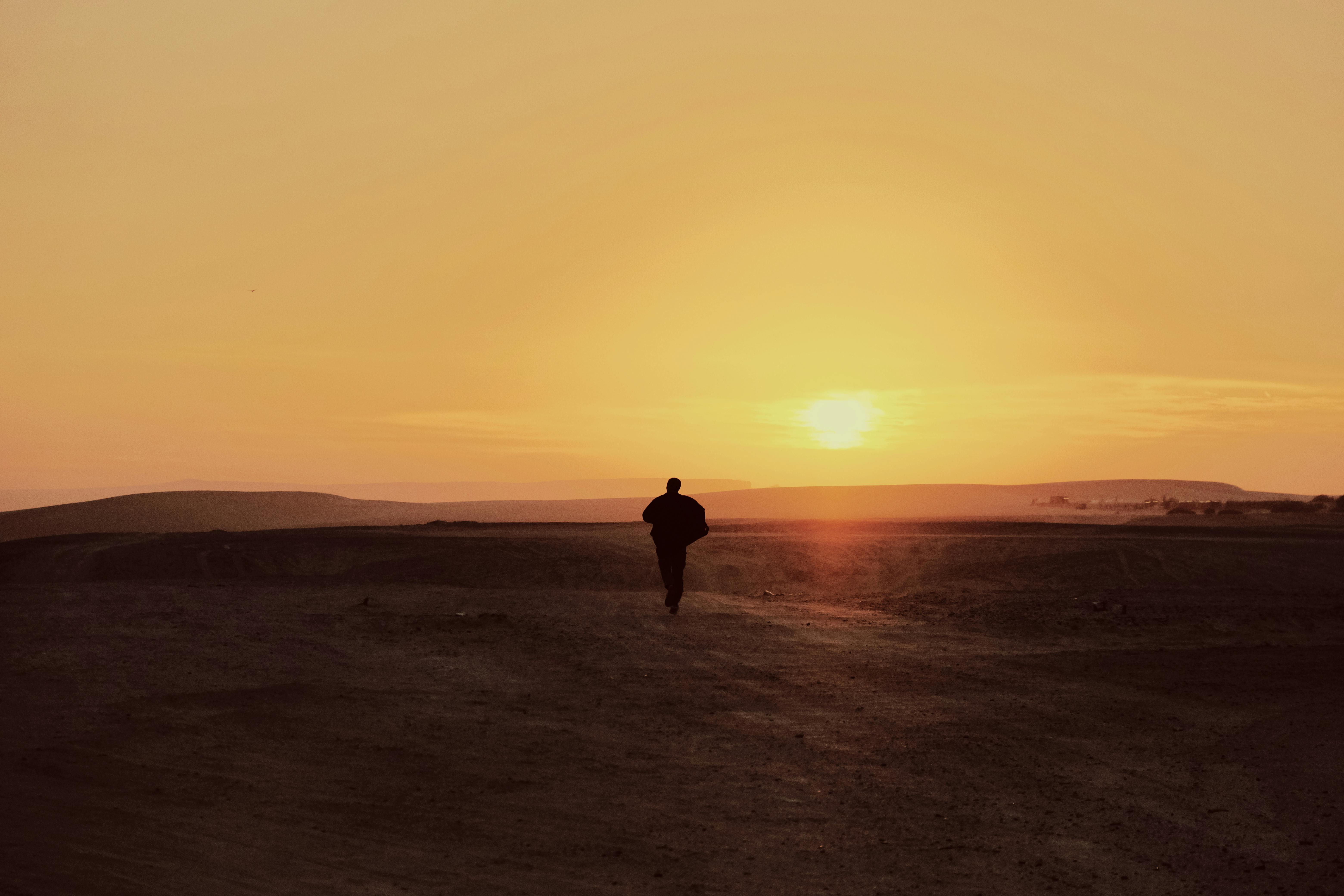 A solitary person walking in a vast desert as the sun sets, creating a warm, serene atmosphere.