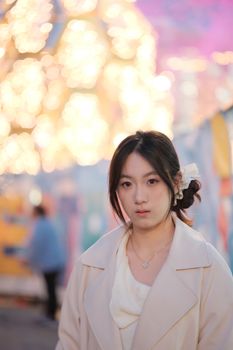 A young woman stands in front of bright festive lights, creating a beautiful bokeh effect.