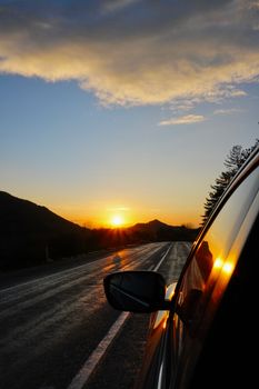 Scenic mountain sunset reflecting on car window, capturing tranquil drive moments.
