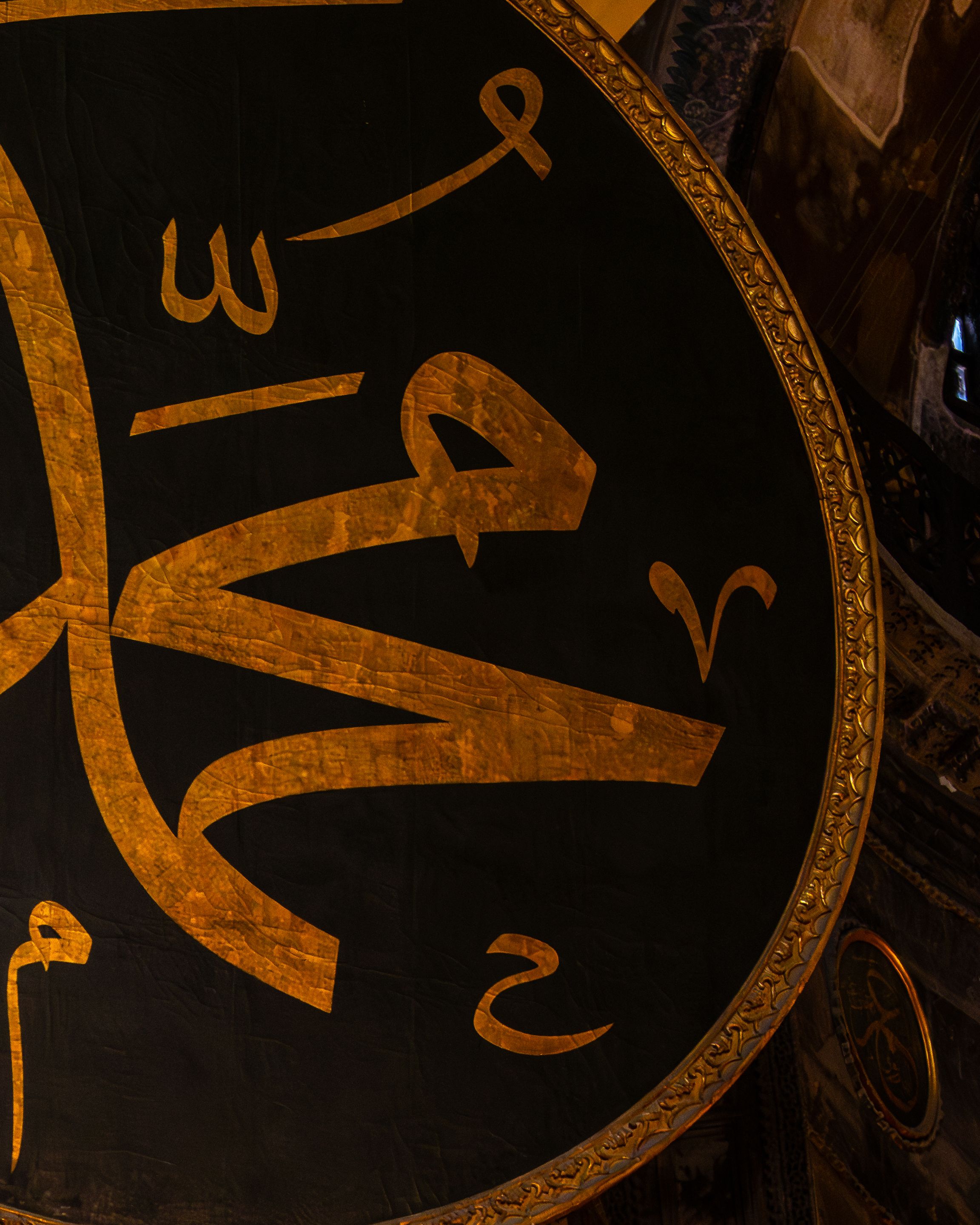Ornate Arabic calligraphy on a circular plaque in a historic, dark interior.
