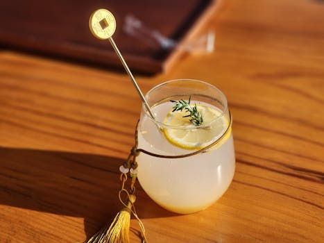 Cocktail al limone freddo con guarnizione di erbe aromatiche e agitatore decorativo su tavolo di legno.
