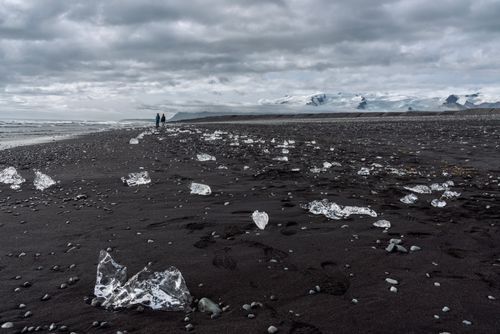 Free Ice fragments scattered on Iceland's iconic black sand beach, with mountains in the distance. Stock Photo