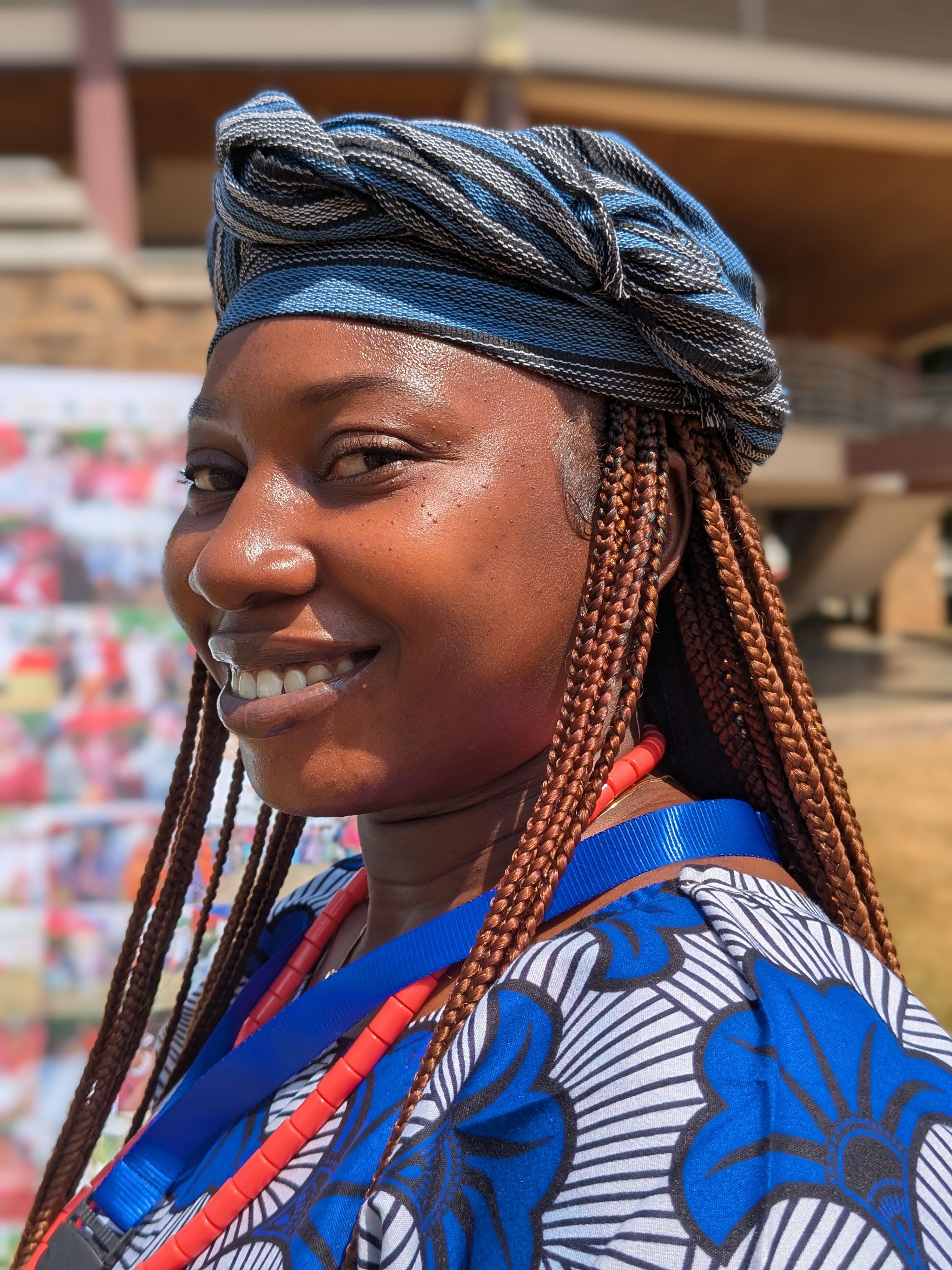 Close-up of a smiling woman in vibrant African traditional attire outdoors.