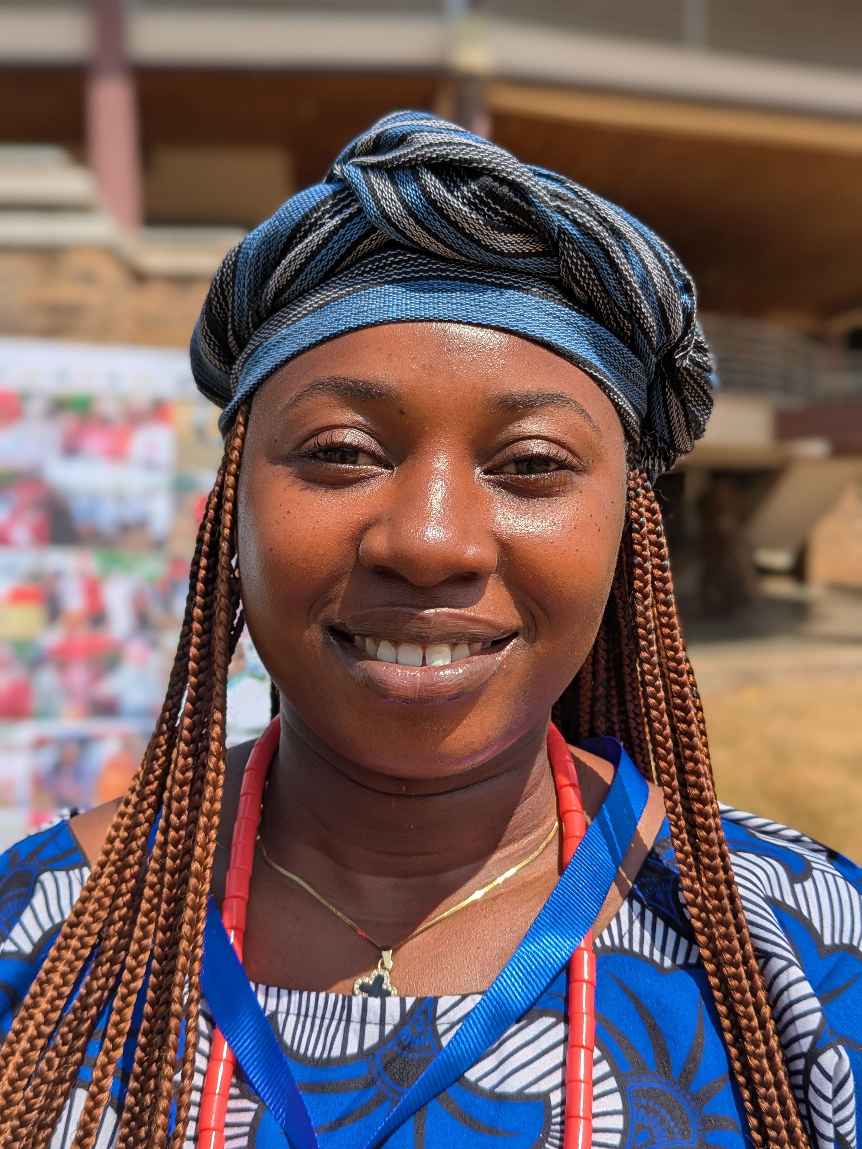Close-up of a smiling woman wearing traditional African clothing and headscarf outdoors.