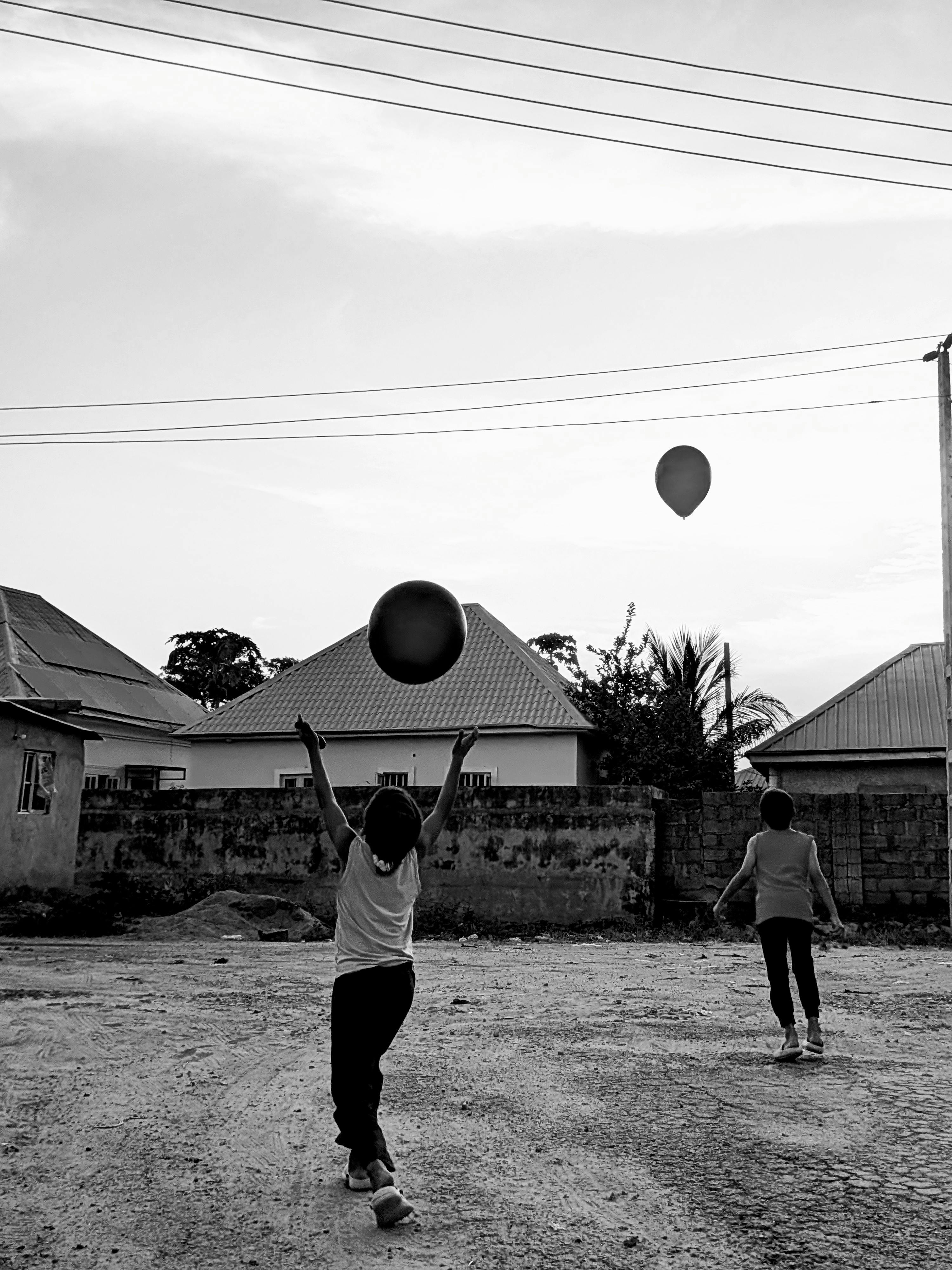 Black and white photo of two children playing with balloons outdoors in Abuja, Nigeria.