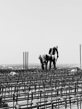 Monochrome image of two workers on a construction site with rebar detailing.