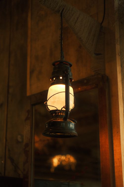 Free Warm glowing vintage lantern hanging indoors in a rustic wooden setting. Stock Photo