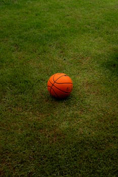 A vibrant orange basketball rests at the center of a lush green grass field.