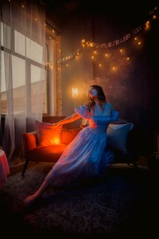 A woman in elegant dress poses in a dimly lit room with fairy lights and a warm ambiance.