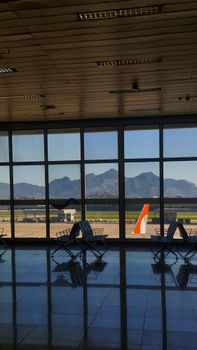 Empty airport terminal overlooking mountains through large windows.