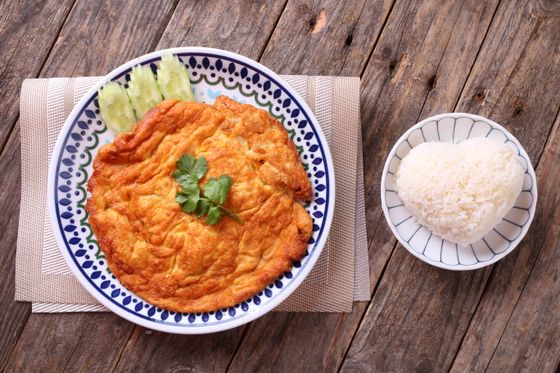 Puffy golden Thai omelette with cilantro and cucumber slices beside a heart-shaped mound of rice