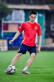 A young man in red sportswear playing soccer on a lush green field in Hanoi, Vietnam.