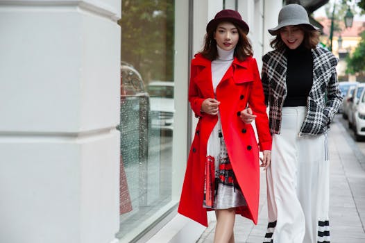 Two stylish women in coats walking along a city street, showcasing modern fashion.
