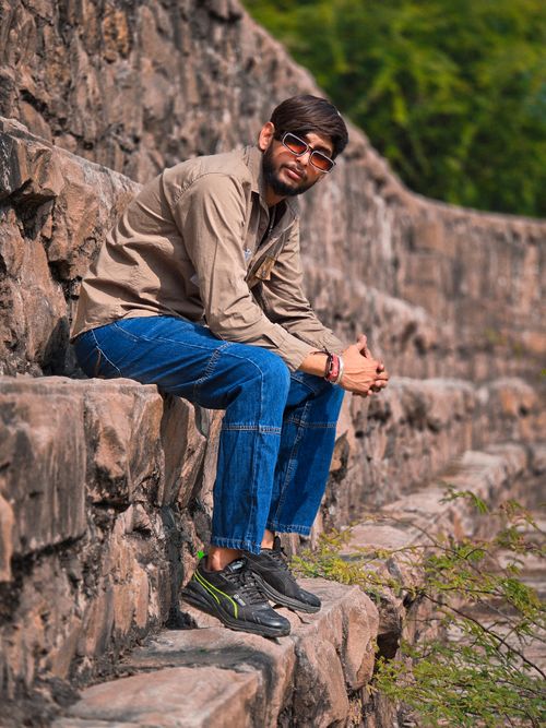 Free A young man sits on stone steps outdoors, wearing sunglasses, casual attire, and sneakers. Stock Photo