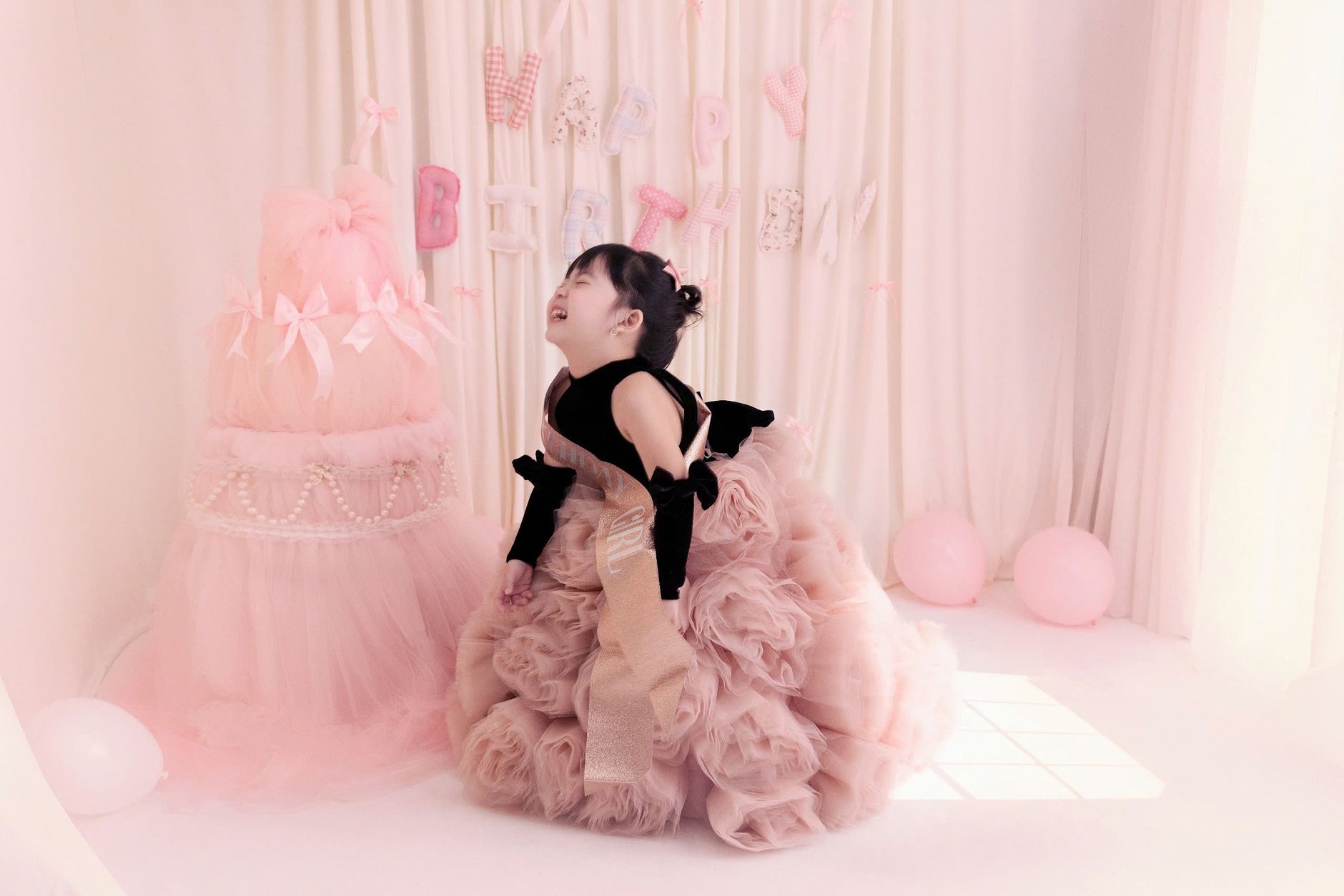 A happy child in a frilly pink dress celebrates a birthday in a pastel-themed room.