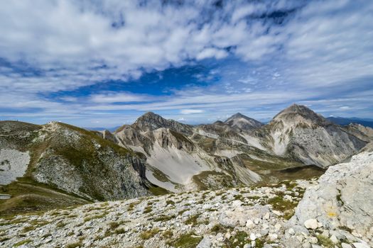 Stunning view of rocky mountain peaks with a bright blue sky filled with scattered clouds.